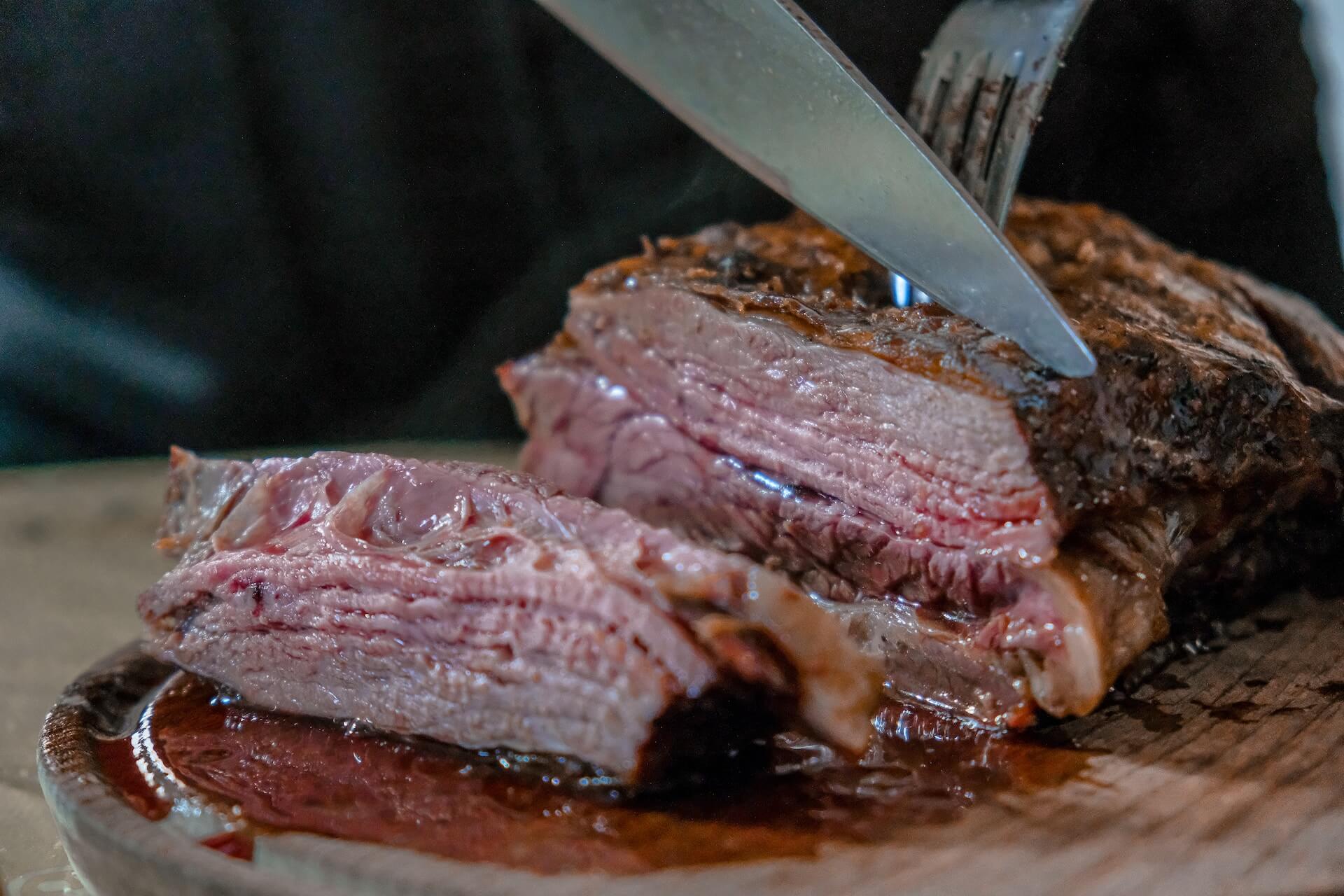 Saftiges Steak, das mit einem Messer geschnitten wird, auf einem hölzernen Schneidebrett.